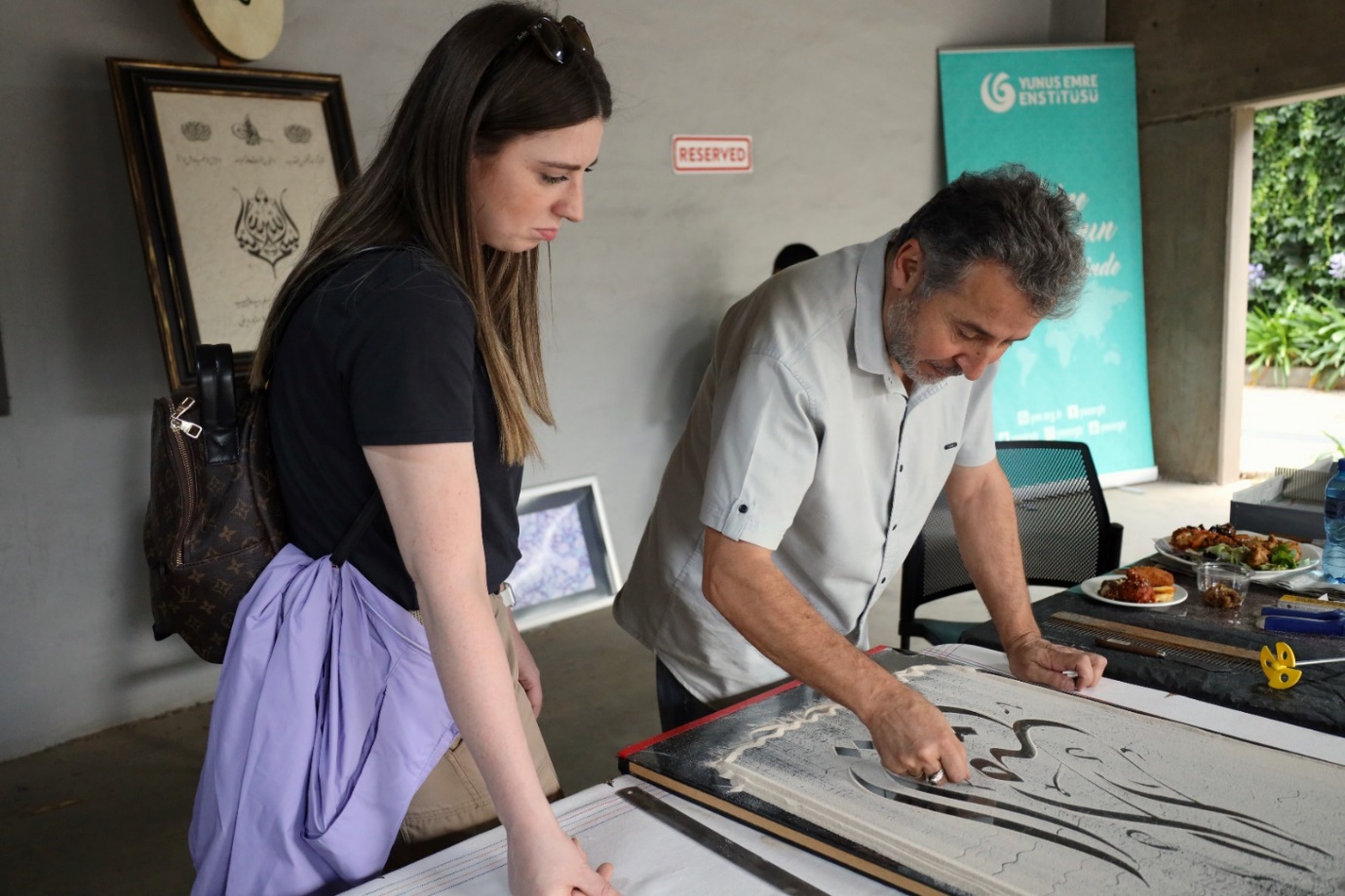 A person and person drawing on a piece of paper

Description automatically generated