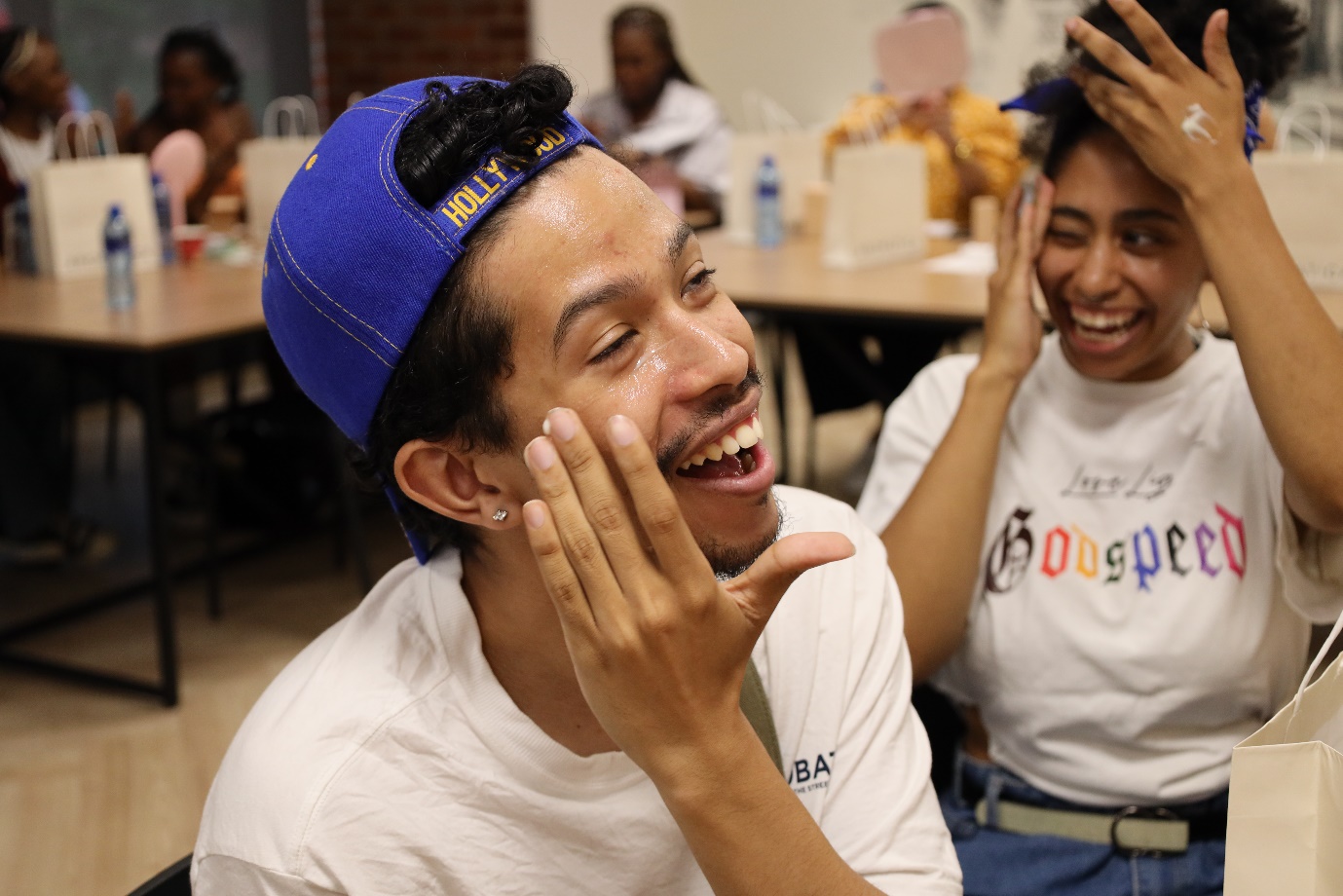 A person in a blue hat laughing
Description automatically generated