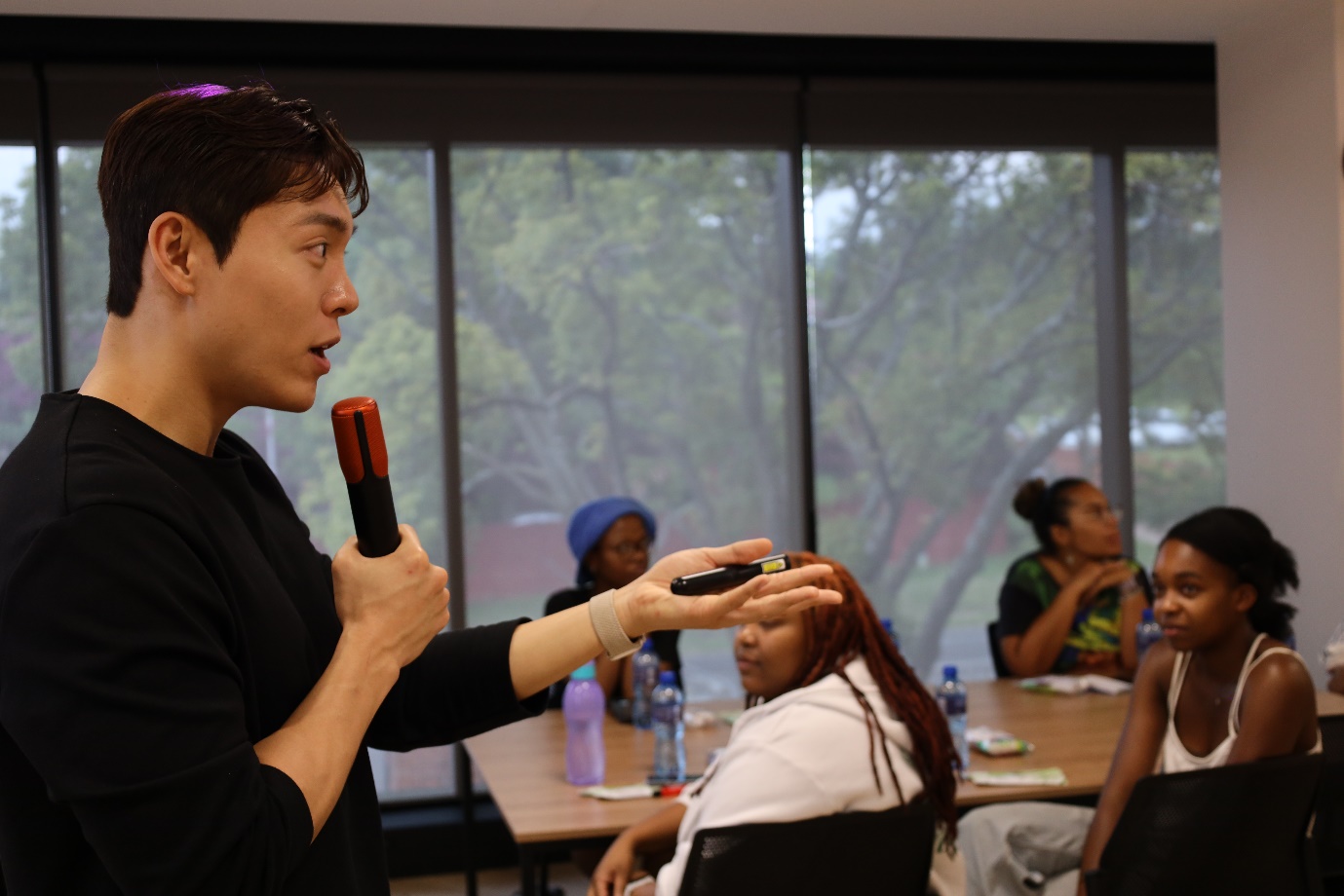 A person holding a microphone in front of a group of people
Description automatically generated