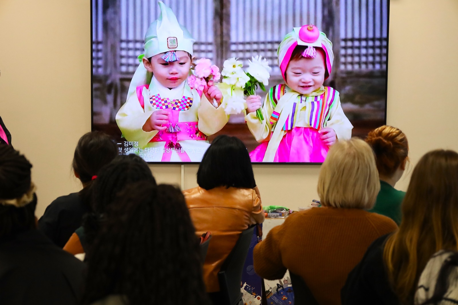 A group of people sitting in a room watching a screen

Description automatically generated