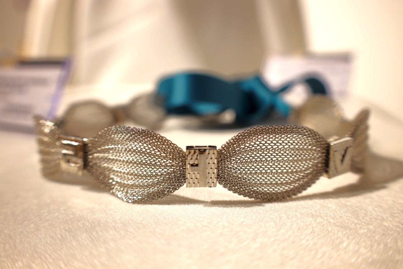 A silver bracelet with a blue ribbon

Description automatically generated