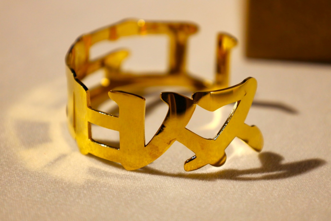 A gold bracelet on a white surface

Description automatically generated