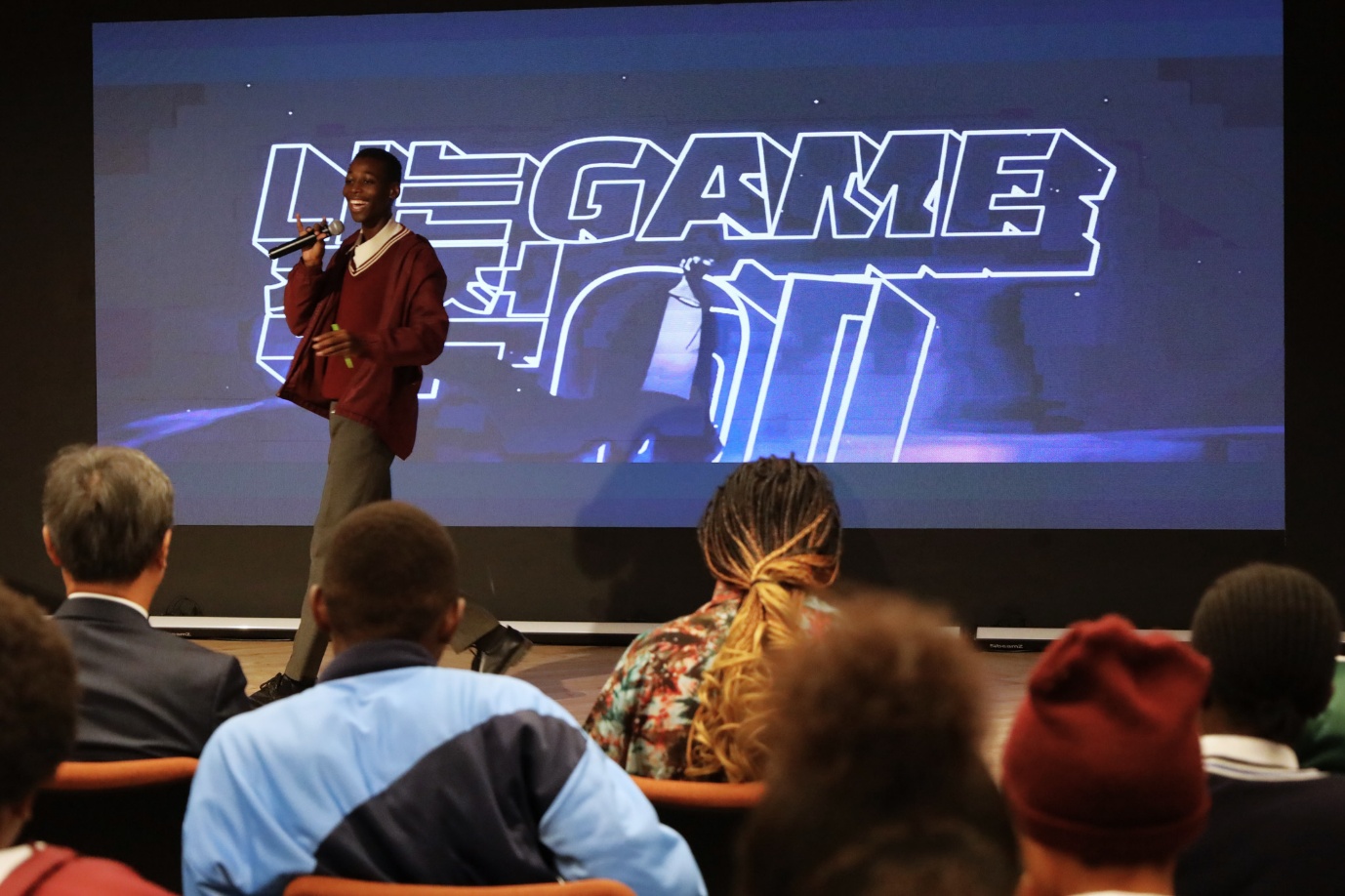 A person speaking into a microphone in front of a large screen

AI-generated content may be incorrect.
